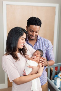 San Francisco Family Photography of Young Dad and Mom in Blush Dress Holding Mixed Race Blended Newborn Son in Nursery in Home