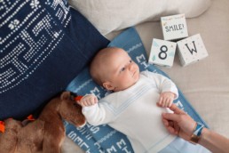San Francisco Family Photography of 8 Week Old Newborn Baby Boy Holding onto Young Dad's Finger Next to Blocks and Horse Stuffed Animal on Blue Handmade Blankets in Home
