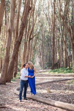 Young Couple Kissing Pregnant Woman in Flowing Royal Blue Dress Surrounded by Eucalyptus Trees in Lover's Lane at the Presidio Park by San Francisco Family Photographer